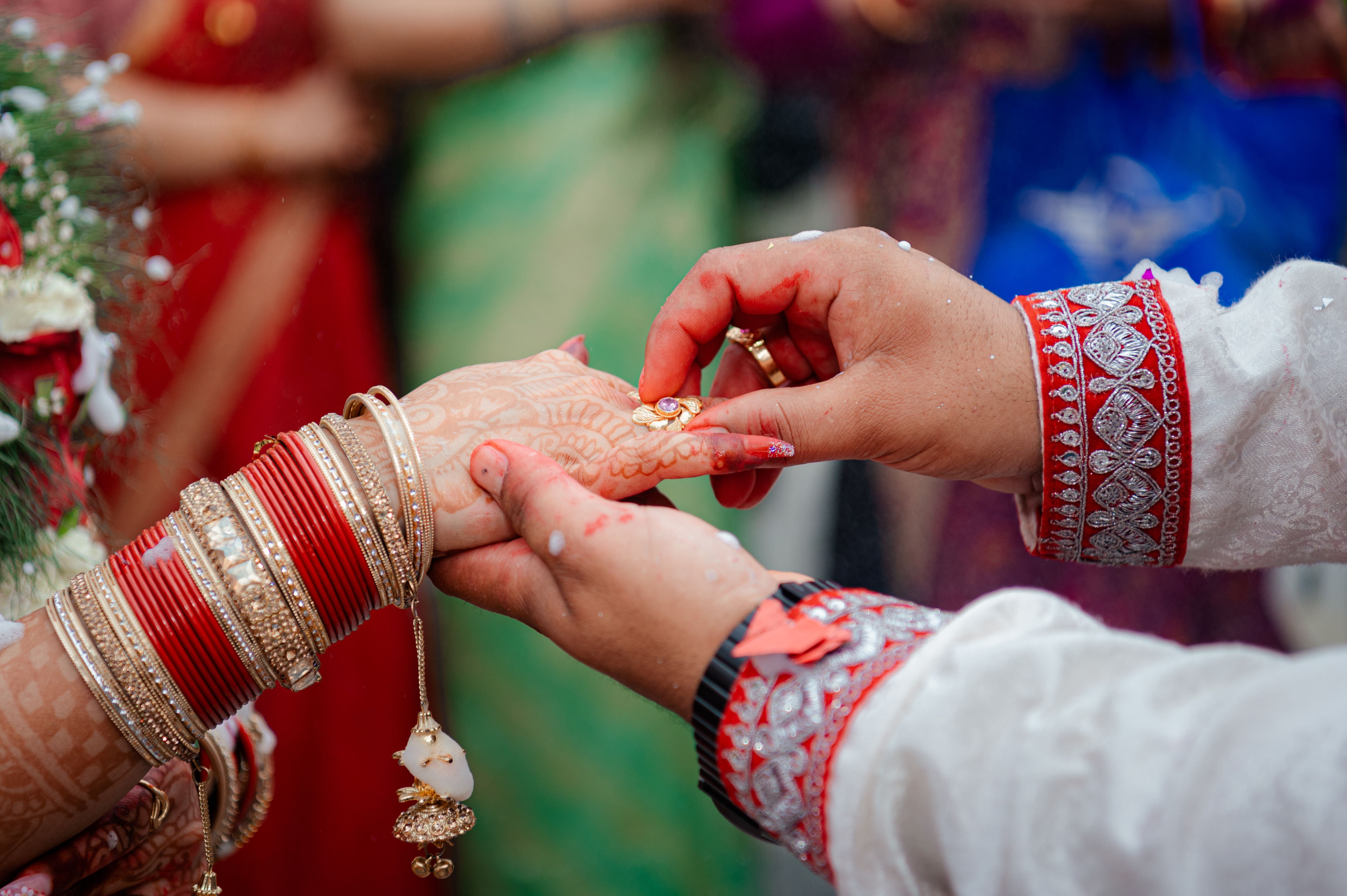 A couple exchanging rings, hands adorned with bangles and henna
